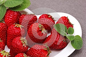 Fresh ripe delicious red strawberries and a green mint leaf on a white plate. healthy dessert