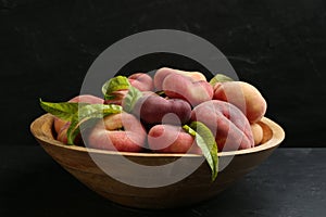 Fresh ripe donut peaches with leaves in bowl on dark table