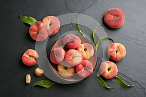 Fresh ripe donut peaches with leaves on dark table, flat lay