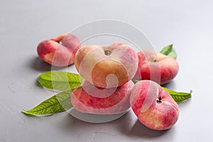 Fresh ripe donut peaches with leaves on light table, closeup