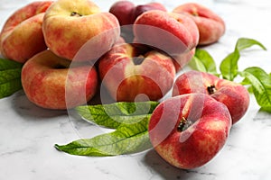 Fresh ripe donut peaches with leaves on white marble table, closeup