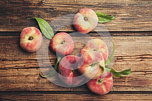 Fresh ripe donut peaches with leaves on wooden table, flat lay