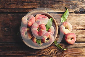 Fresh ripe donut peaches with leaves on wooden table, flat lay