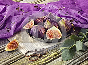 Fresh ripe figs in vintage plate, green eucalyptus branch, viney scissors, purple shawl as decor.