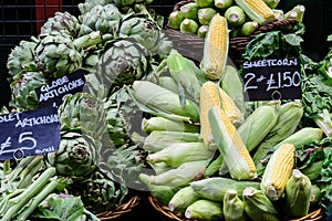 Fresh ripe fresh organic globe artichokes and yellow sweet corn displayed for sale at a street food market, side view of healthy v