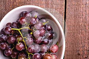 Fresh ripe grape berries in bowl on brown wooden background