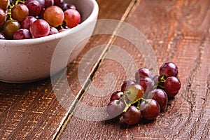 Fresh ripe grape berries in bowl on brown wooden background