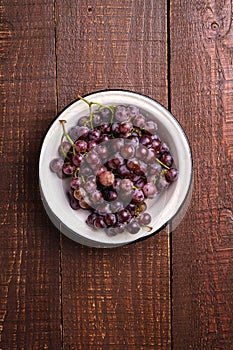 Fresh ripe grape berries in bowl on brown wooden background