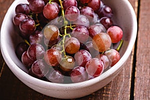 Fresh ripe grape berries in bowl on brown wooden background