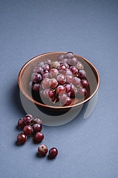 Fresh ripe grape berries in brown wooden bowl on blue grey minimal background