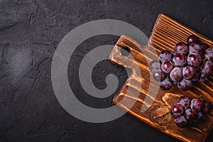Fresh ripe grape berries on brown wooden cutting board on dark stone background