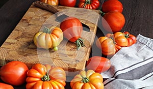 Fresh ripe hairloom tomatoes and knife on rustic wooden board over dark background