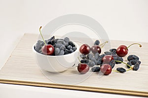 Fresh ripe honeysuckle berries and cherry in a ceramic bowl on a wooden board. Healthy breakfast. White bowl of honeysuckle.