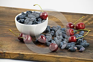 Fresh ripe honeysuckle berries and cherry in a ceramic bowl on a wooden board. Healthy breakfast. White bowl of honeysuckle.