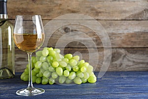 Fresh ripe juicy grapes and wine on blue table against wooden background