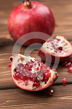 Fresh, ripe, juicy pomegranate fruit is divided into pieces on a brown wooden background
