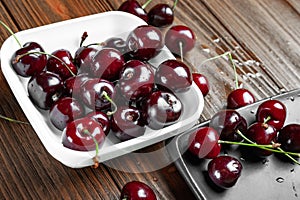 Fresh ripe juicy sweet cherries in white and black plates on a wooden background. Wet sweet cherry with water droplets