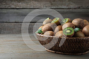 Fresh ripe kiwis in wicker bowl on wooden table, space for text