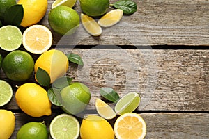Fresh ripe lemons, limes and green leaves on wooden background, flat lay. Space for text