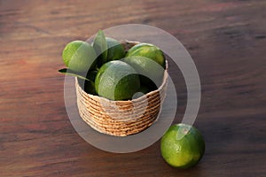 Fresh ripe limes in wicker basket on wooden table