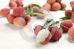 Fresh ripe lychees with leaves on white wooden table, closeup. Space for text