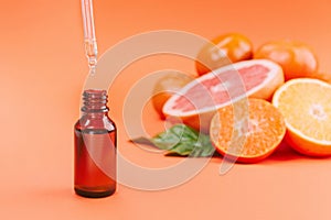 Fresh ripe mandarins, grapefruit and oranges with green leaves and glass bottle with essential oil on orange background