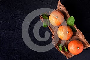Fresh ripe mandarins with mint on wood bark bowl, orange textile on black background. Modern dark mood style. Horizontal banner. C