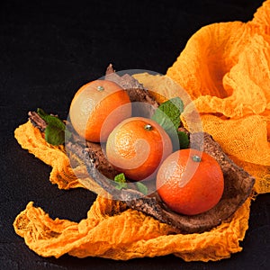 Fresh ripe mandarins with mint on wood bark bowl, orange textile on black background. Modern dark mood style. Horizontal banner. C