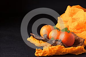 Fresh ripe mandarins with mint on wood bark bowl, orange textile on black background. Modern dark mood style. Horizontal banner. C