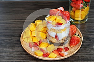 Fresh ripe mango and strawberry fruit in a cup with cookies, soy yogurt on a wooden plate
