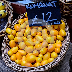 Fresh ripe orange kumkuat fruits displayed with black label and price in a wooden box, at a street food market, ready to eat exoti