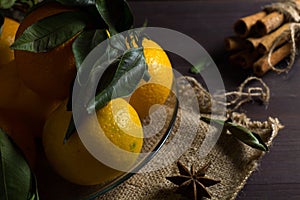 Fresh orange tangerines with green leaves on wooden background. ripe fruits on dark table with sticks of cinnamon and spices.