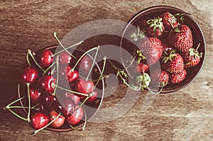 Fresh ripe organic cherries and strawberry on wooden background. Vintage rustic style and color tinting.