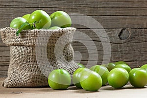 Fresh ripe organic green plums or greengage in burlap sack on wooden background