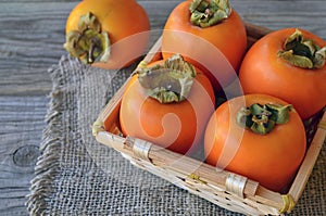 Fresh ripe organic Persimmon or Kaki fruit in a basket on old wooden table.Diospyros kaki.