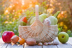 Fresh ripe organic vegetables and fruits in a wicker basket on a wooden table in the garden