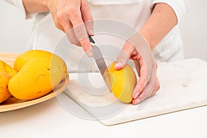 Fresh ripe organic yellow mangoes close up. Woman cutting mango on white cutting board