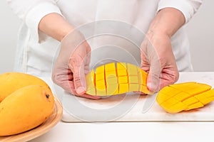 Fresh ripe organic yellow mangoes close up. Woman cutting mango on white cutting board