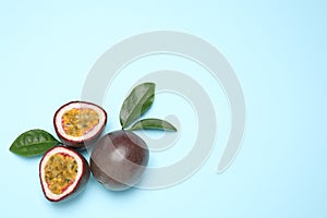 Fresh ripe passion fruits maracuyas with green leaves on light blue background, flat lay. Space for text