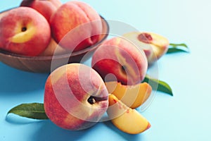 Fresh ripe peaches and green leaves on light blue background, closeup