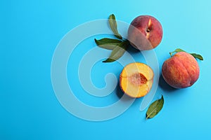 Fresh ripe peaches and green leaves on light blue background, flat lay. Space for text