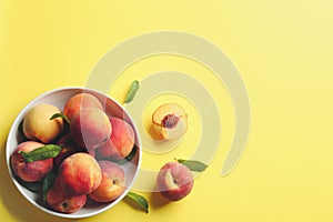 Fresh ripe peaches and green leaves on yellow background, flat lay. Space for text