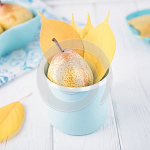 Fresh ripe pear and yellow autumn leaves in enameled cup on a white background. Toned photo. Copy space