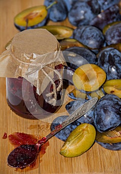 Fresh ripe plum - raw materials for making homemade jam and a glass jar with jam