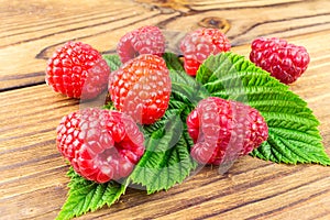 Fresh, ripe raspberries on leaves, rustic wooden background.