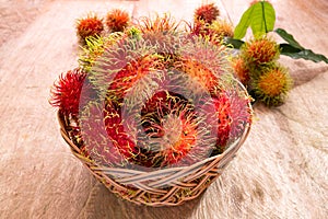 Fresh ripe red rambutans fruit in basket on wood floor