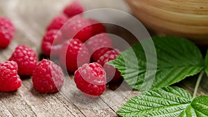 Fresh ripe red raspberries with leaves in a bowl on rustic old wooden table in 4K VIDEO.
