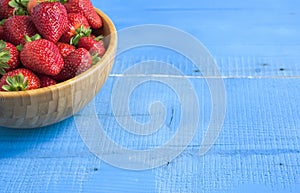 Fresh ripe red strawberries in bowl on blue rustic wooden table.