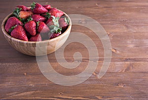 Fresh ripe red strawberries in bowl on rustic wooden table.