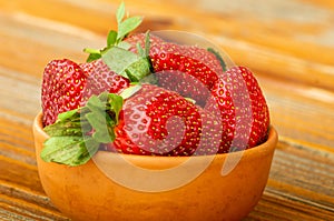 Fresh ripe red strawberries in a clay bowl on an old wooden table,outdoor